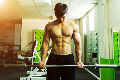 Shirtless muscular man lifting weights while exercising at gym