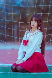 Portrait young woman sitting against net on soccer field