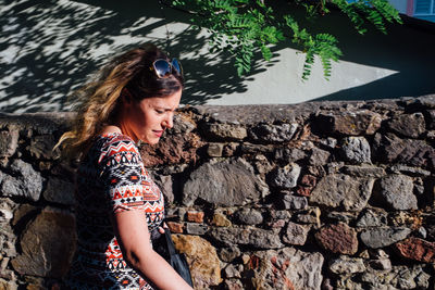 Side view of young woman walking by stone wall