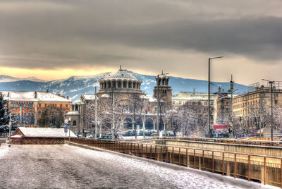 Road by buildings in city against sky during winter