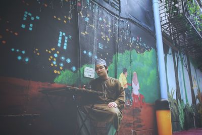 Portrait of young man looking away while sitting on illuminated glass