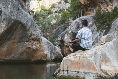 Young man sitting on rock against waterfall