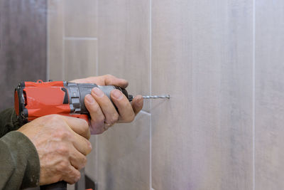 Close-up of man holding drill machine against wall