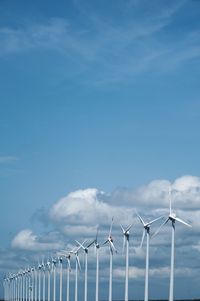 Wind turbines by fence against sky