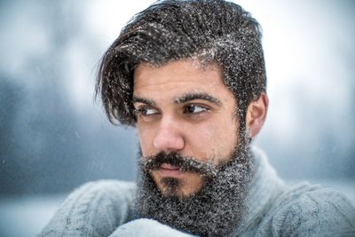 Thoughtful bearded man looking away during snowfall