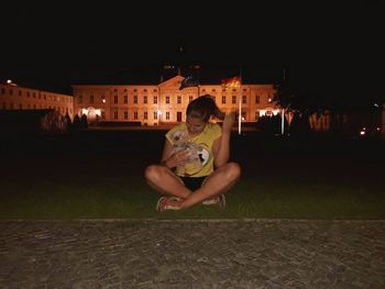 Portrait of man sitting on illuminated city at night