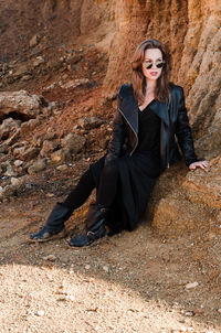 Portrait of woman wearing sunglasses sitting by rock formation outdoors