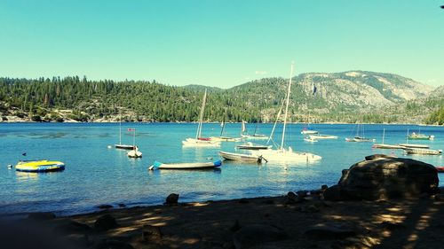 Boats moored on sea against clear blue sky