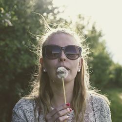 Woman wearing sunglasses holding dandelion