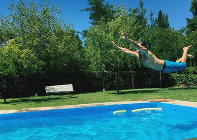 Man jumping in swimming pool against trees