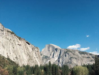 Low angle view of rocky mountains against clear blue sky on sunny day