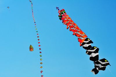 Low angle view of red flags hanging against clear blue sky