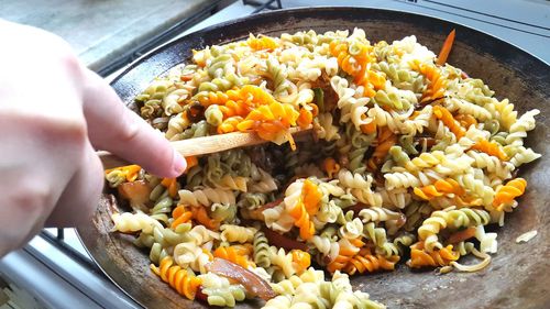 Cropped image of person cooking fusilli pasta at home