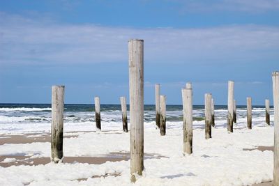 Wooden posts on beach against sky during winter