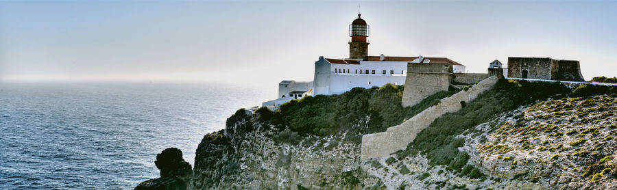 Lighthouse by sea and buildings against sky