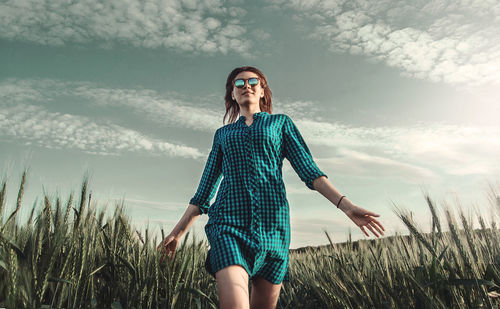 Young woman standing on field against sky