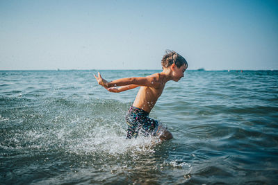 Shirtless boy playing in water against sky