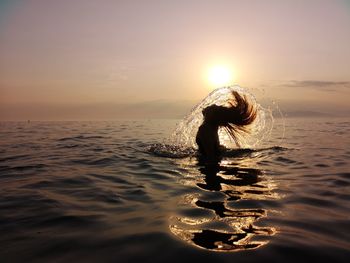 Woman tossing hair in sea against sky during sunset