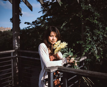 Young woman sitting on railing against trees