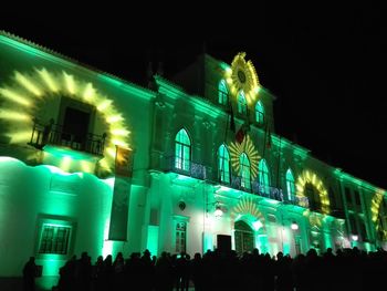 People at illuminated building against sky at night