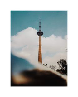 Communications tower in city against cloudy sky