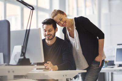 Happy businesswoman with male colleague using computer in office