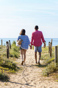 Back view of a young couple walking to beach while holding hands