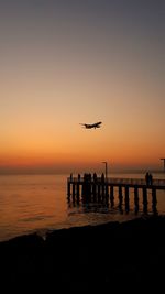 Silhouette airplane flying over sea against sky during sunset