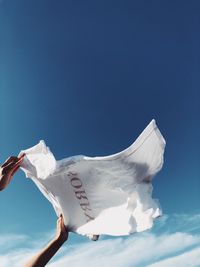 Cropped hand holding t-shirt against sky