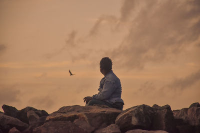 Rear view of man standing on rock against sky during sunset