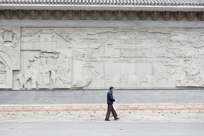Side view of man walking against carvings on wall