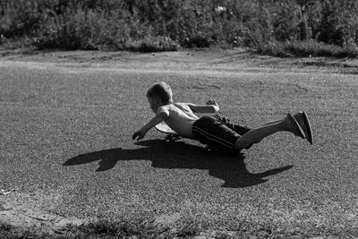 Rear view of shirtless boy levitating over road during sunny day