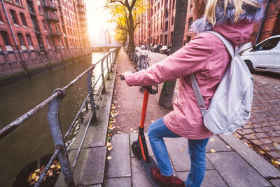 Rear view of woman with push scooter on footpath