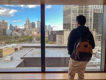 Rear view of man looking at window view of buildings and urban skyline.