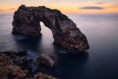 Rock formation in sea against sky during sunset