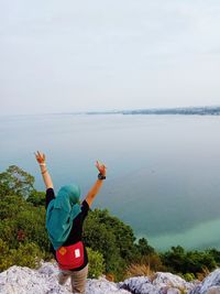 Woman gesturing at beach against sky