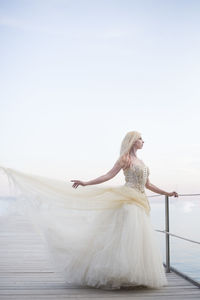 Woman standing on white railing against sky