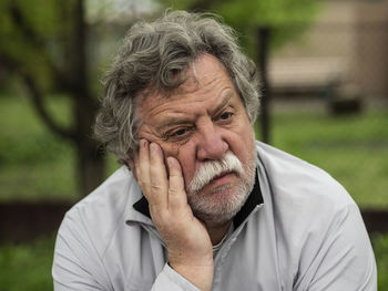 Close-up of sad senior man with hand on chin sitting in park