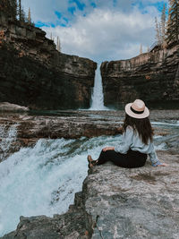 Woman sitting on rock by waterfall at crescent falls, alberta.