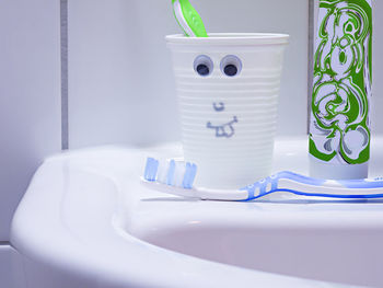 Close-up of toothbrush by disposable cup on sink at home