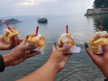 Cropped image of hand holding ice cream against sea