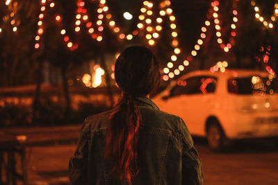 Rear view of woman standing on illuminated street at night