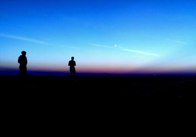 Silhouette people on landscape against blue sky