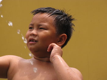 Water splashing on shirtless boy against wall