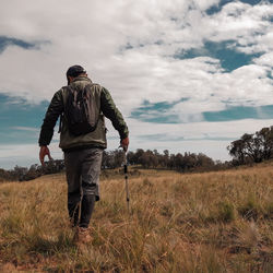 Rear view of man walking on field against sky