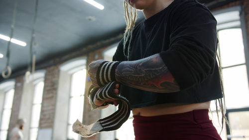 Midsection of woman wrapping band on arm at gym