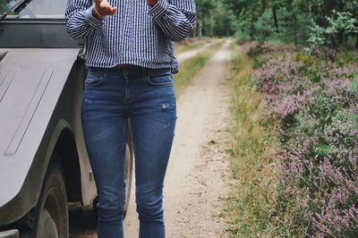 Midsection of woman standing on land by car and plants