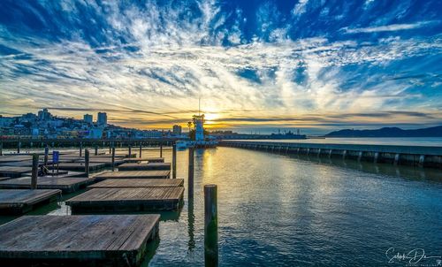 Pier over river against sky during sunset