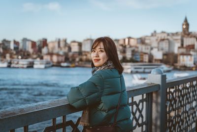 Portrait of woman standing by railing against cityscape