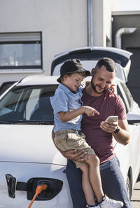 Father and son checking smartphone by charging electric car